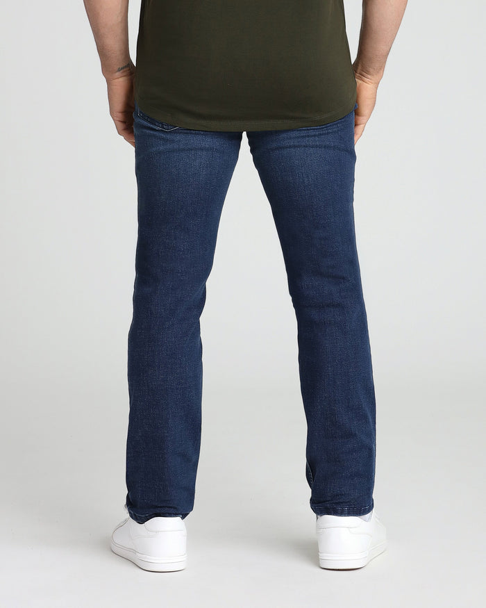 Man wearing olive green t-shirt and medium blue athletic fit jeans with white sneakers, shown from behind.