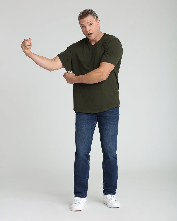 Man wearing olive green v-neck t-shirt and medium blue athletic fit jeans with white sneakers.