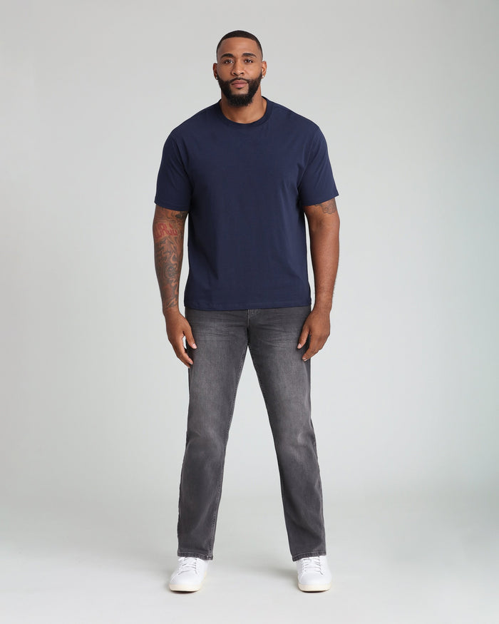 Man wearing navy short-sleeve t-shirt and gray athletic fit jeans with white sneakers.