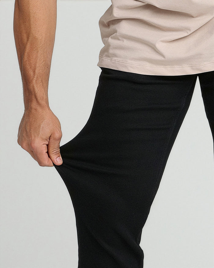 Black athletic fit pants with tapered leg, worn with cream-colored shirt.