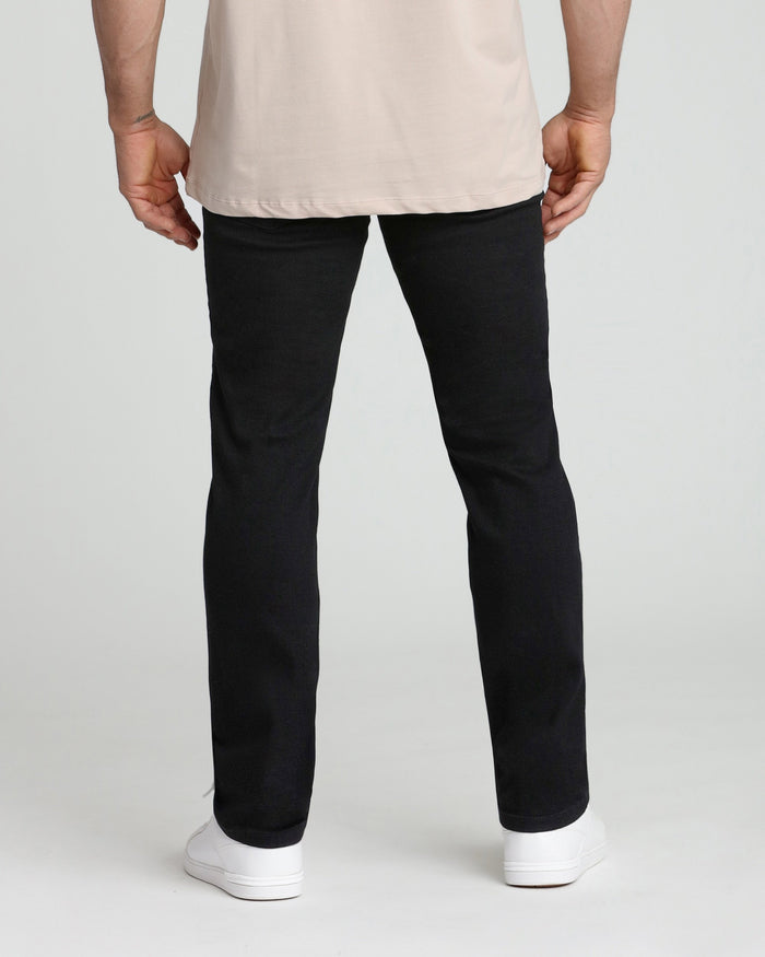 Man wearing cream t-shirt and black athletic fit jeans with white sneakers, shown from behind.