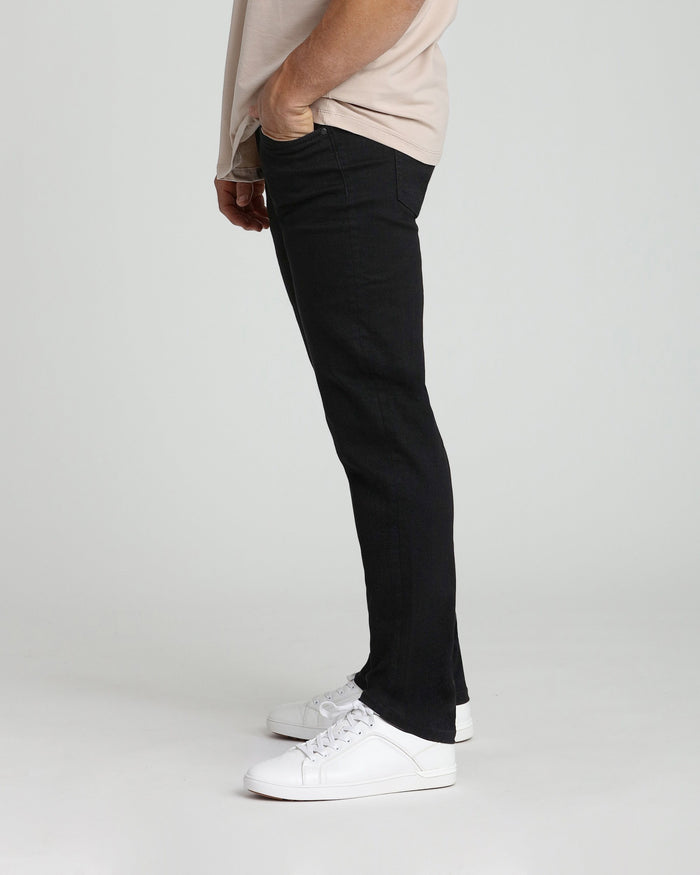 Black athletic fit jeans on model wearing beige shirt and white sneakers.