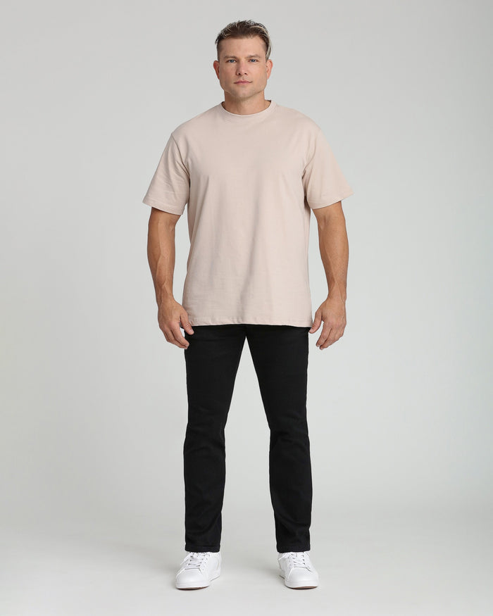Man wearing beige short-sleeve t-shirt and black athletic fit jeans with white sneakers.