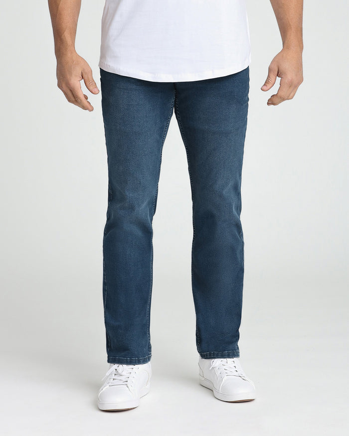 Man wearing white t-shirt and midnight blue athletic fit jeans with white sneakers.