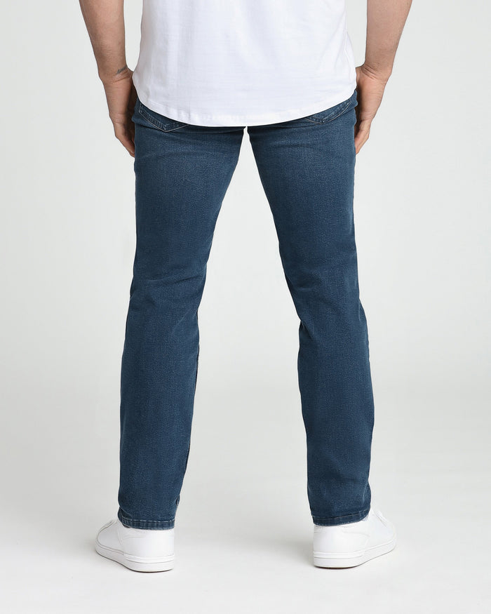 Man wearing white t-shirt and midnight blue athletic fit jeans with white sneakers, back view.