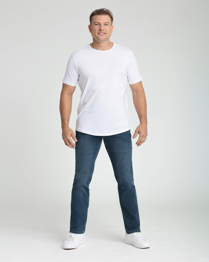 Man wearing white crew-neck short-sleeve t-shirt and dark blue denim jeans with white sneakers.
