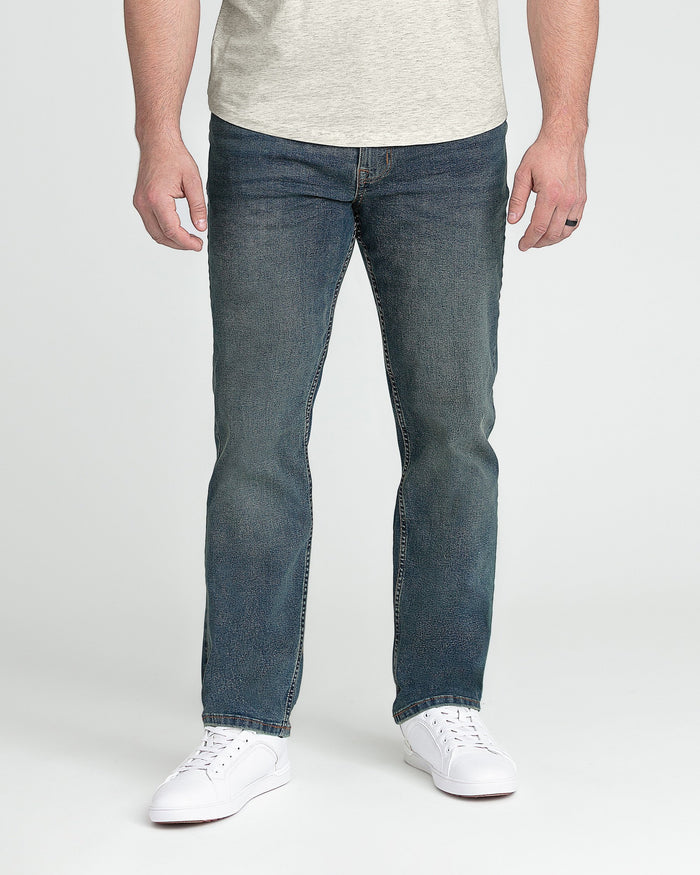 Man wearing light gray t-shirt and dark tinted denim jeans with white sneakers.