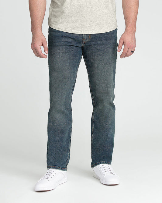 Man wearing light gray t-shirt and dark tinted denim jeans with white sneakers.