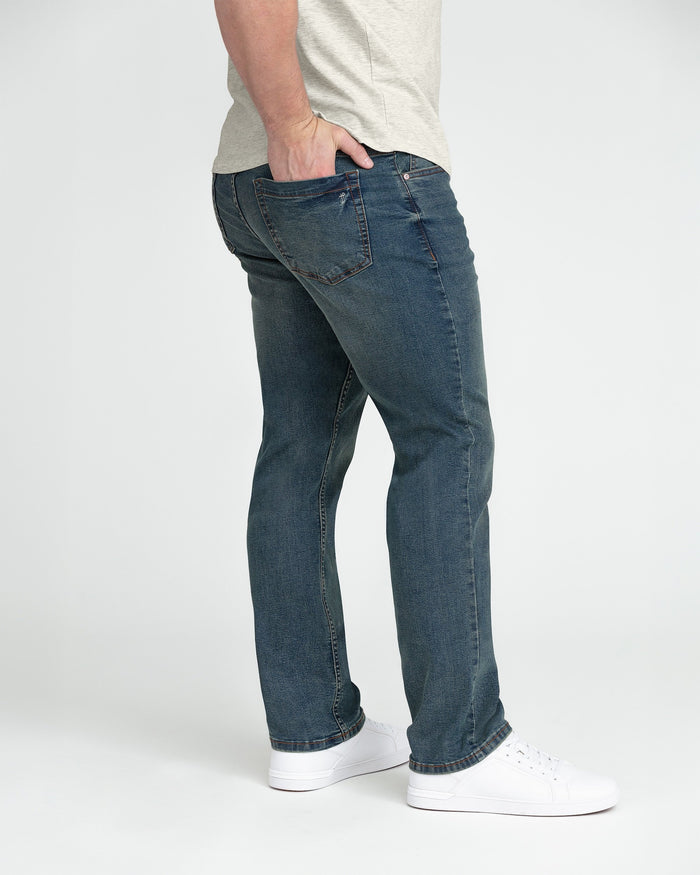 Man wearing tinted blue denim cowboy jeans with athletic fit and white sneakers.