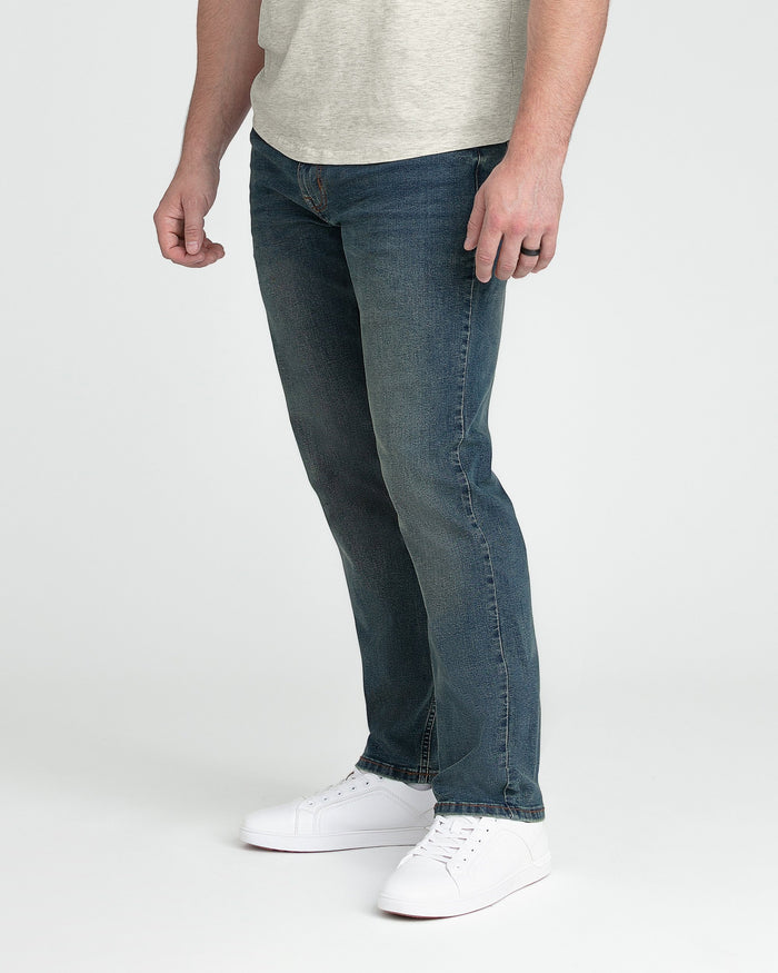 Man wearing light gray t-shirt and dark blue athletic fit jeans with white sneakers.
