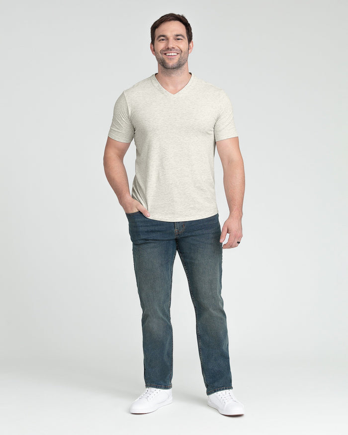 Man wearing cream heathered v-neck t-shirt and medium wash denim jeans with white sneakers.
