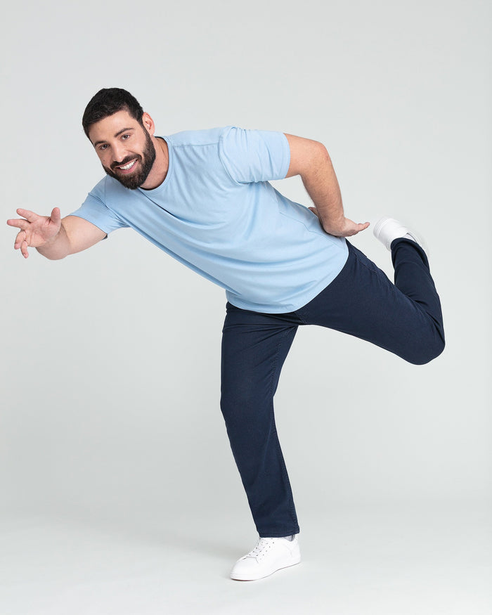 Man wearing light blue sleeveless athletic shirt and navy pants with white sneakers in dynamic pose.
