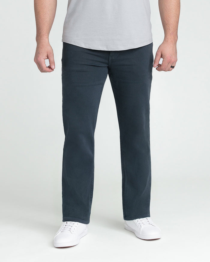 Man wearing light gray t-shirt and dark slate athletic fit jeans with white sneakers.