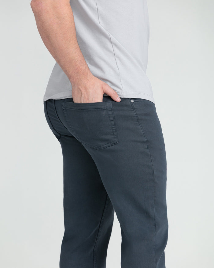 Man wearing light gray t-shirt and dark slate athletic fit pants with hand in pocket.