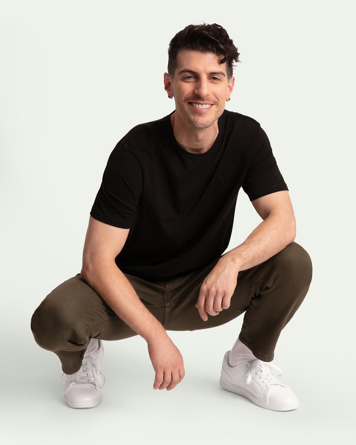 Man wearing black short-sleeve t-shirt and olive athletic fit pants with white sneakers.