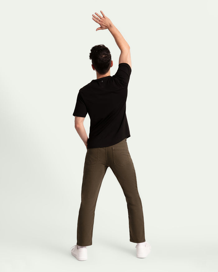 Man wearing black t-shirt and olive athletic fit pants with white socks, shown from behind.