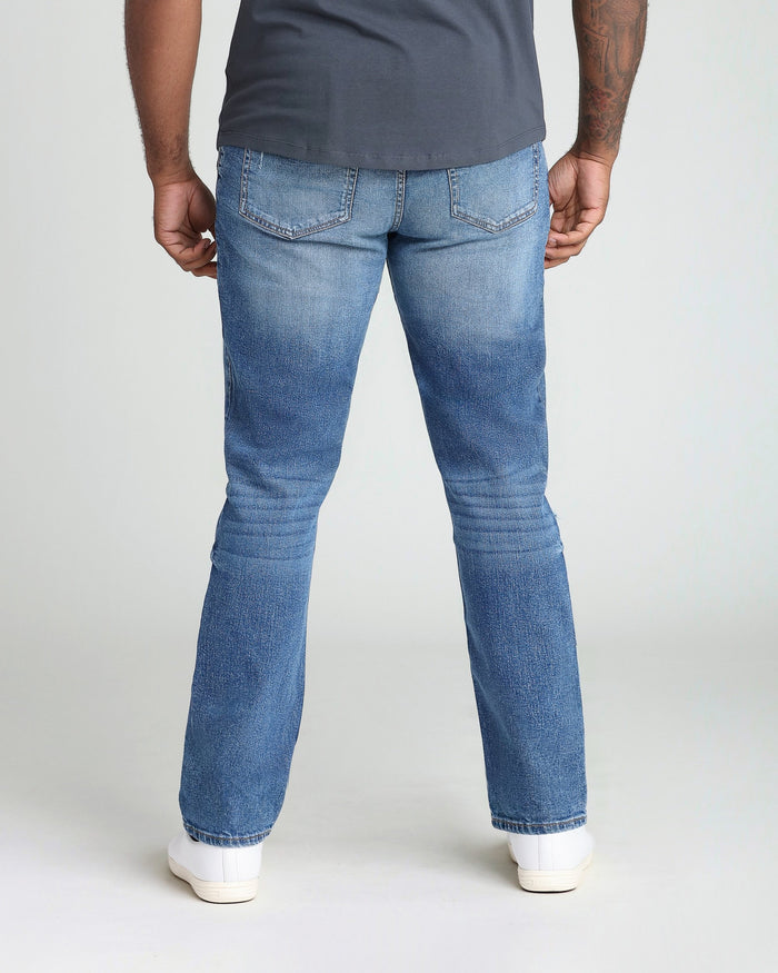 Medium blue ripped athletic fit jeans shown from back, worn with gray t-shirt and white sneakers.