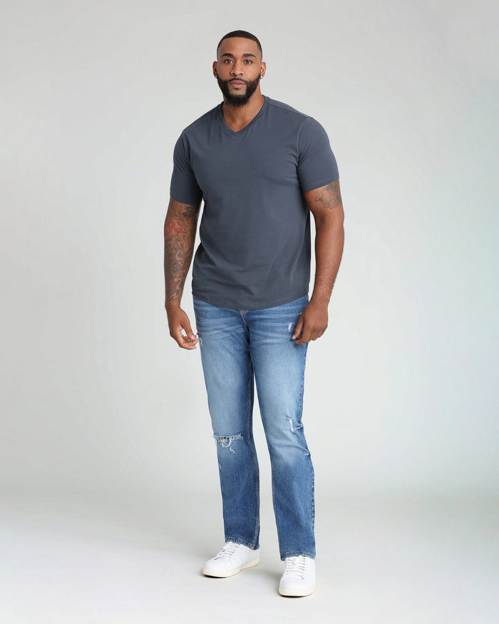 Man wearing charcoal v-neck t-shirt and medium blue ripped jeans with white sneakers.