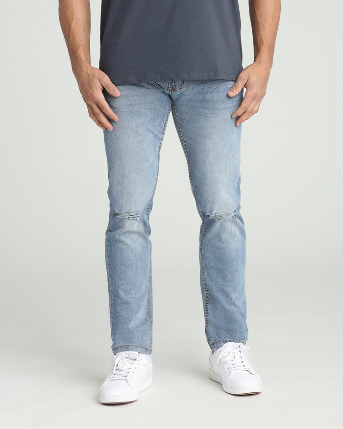 Light blue ripped jeans in athletic fit with distressed knee details, worn with dark shirt and white sneakers.