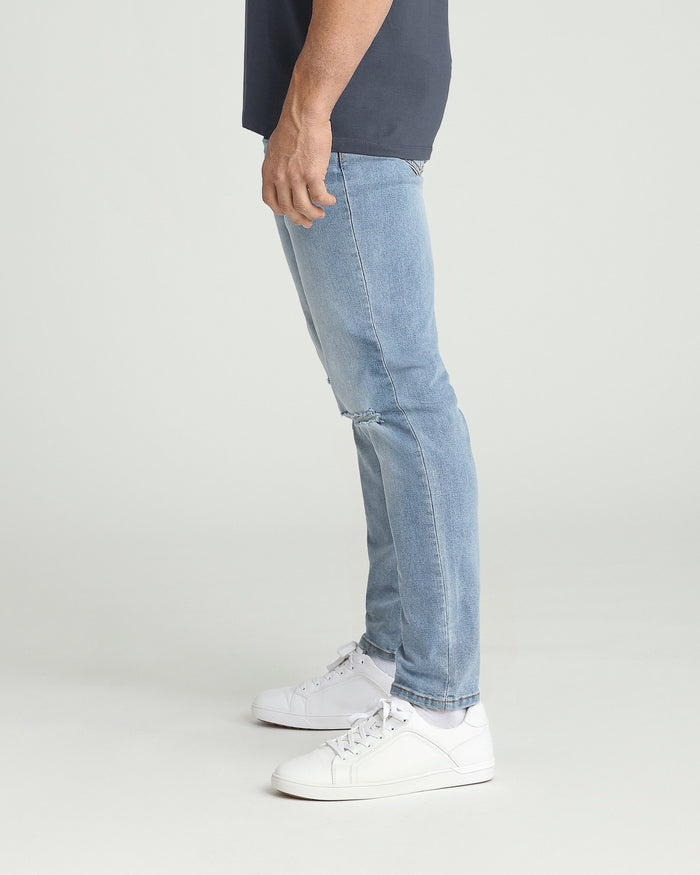 Light blue athletic fit jeans with ripped knee detail, shown on model wearing white sneakers.