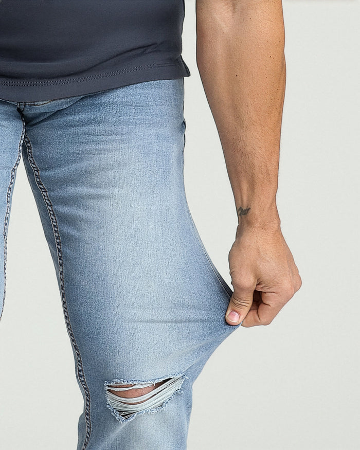 Light blue ripped jeans with athletic fit, featuring a large tear on the thigh and visible stitching details.