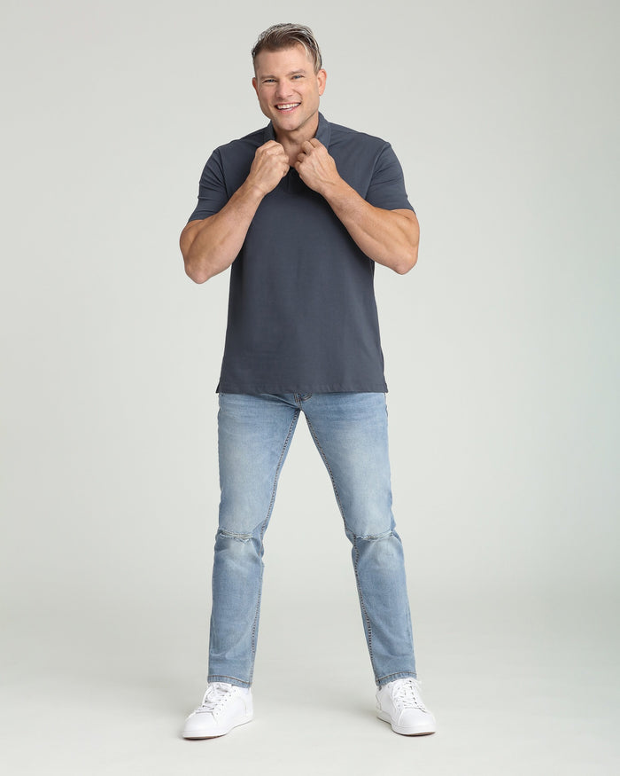 Man wearing dark blue athletic fit polo shirt with light-wash ripped jeans and white sneakers.
