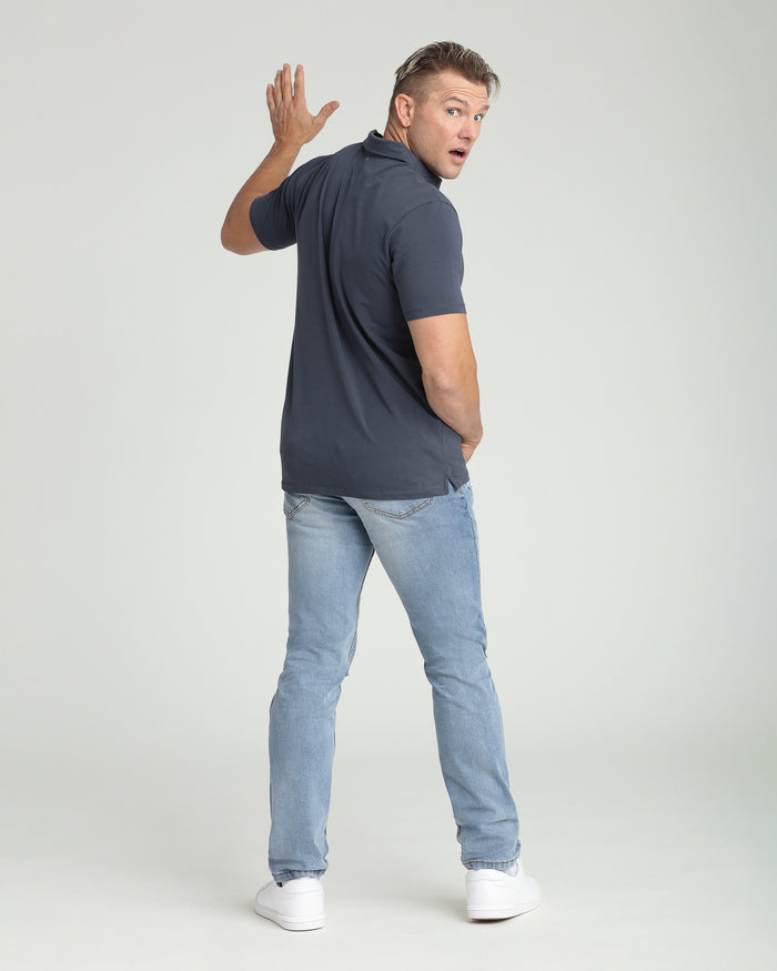 Man wearing dark blue athletic fit polo shirt and light wash ripped jeans, shown from behind.