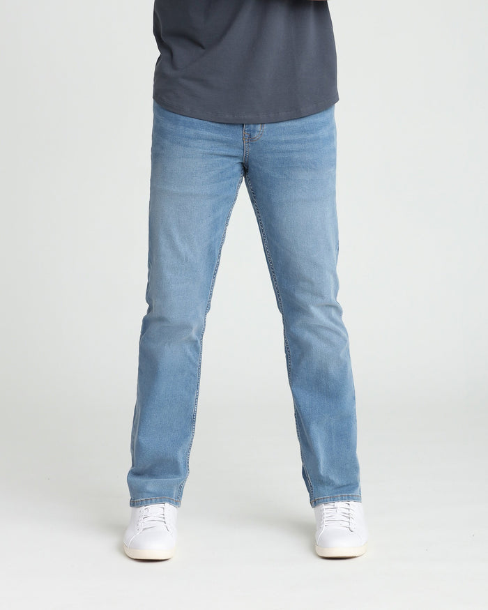 Light indigo athletic fit jeans on model wearing dark navy top and white sneakers.