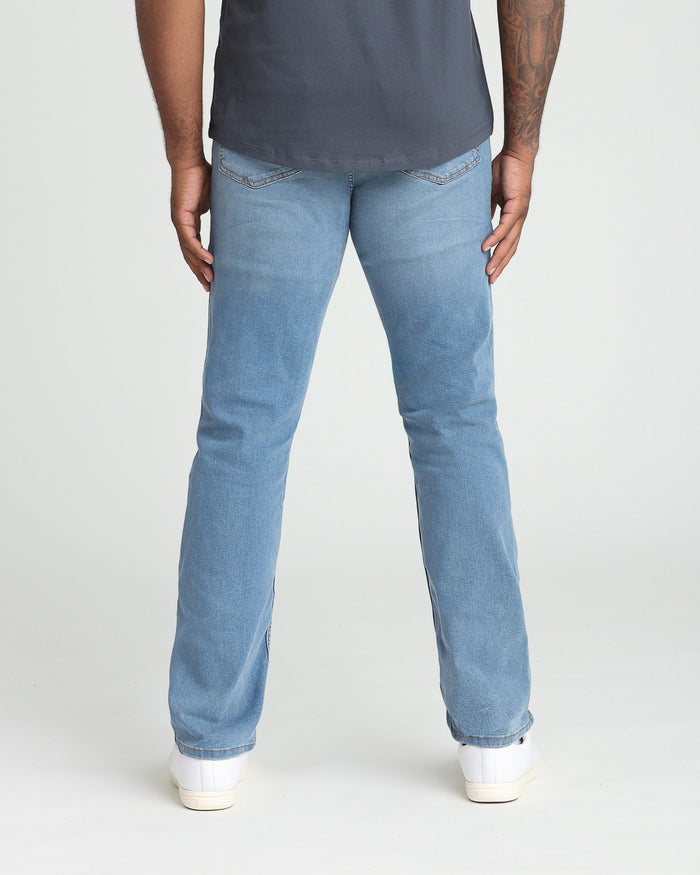 Man wearing dark navy t-shirt and light indigo athletic fit jeans with white sneakers, rear view.