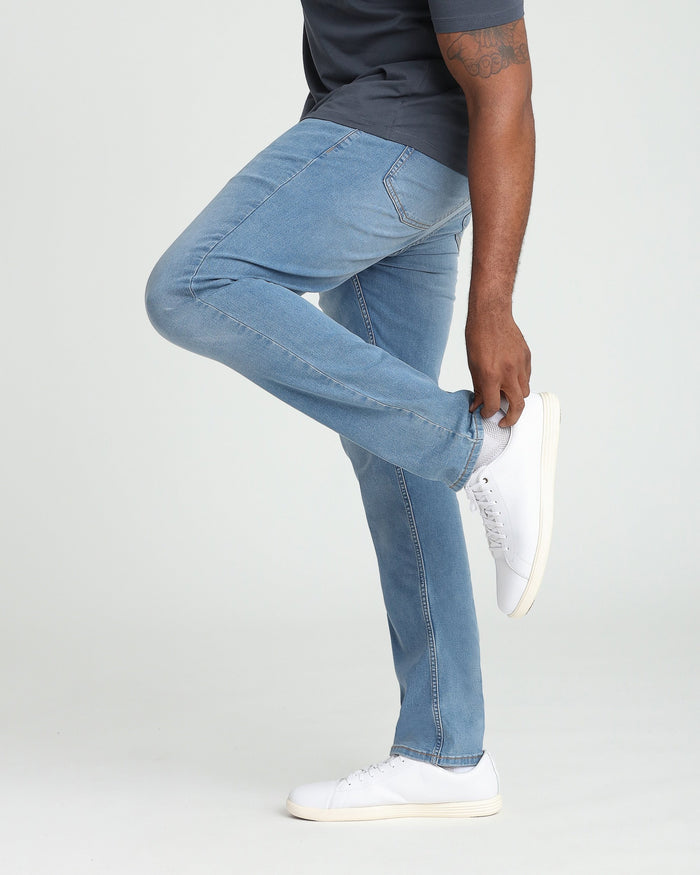 Light indigo athletic fit jeans on a model wearing a dark t-shirt and white sneakers.