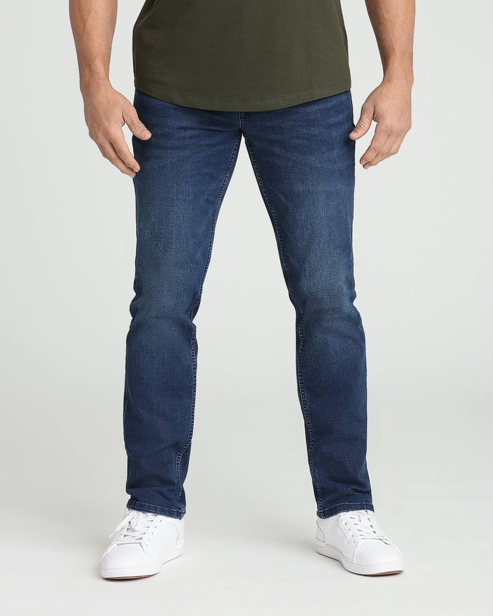 Man wearing dark blue athletic fit jeans with olive green shirt and white sneakers.
