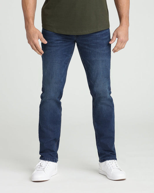 Man wearing dark blue athletic fit jeans with olive green shirt and white sneakers.