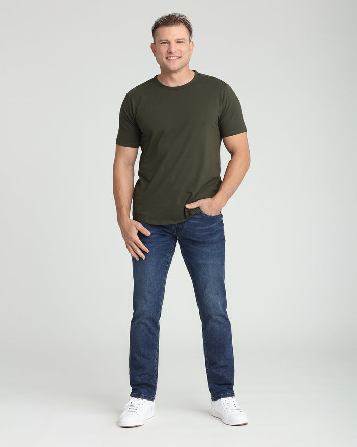 Man wearing olive green short-sleeve t-shirt and dark blue athletic fit jeans with white sneakers.