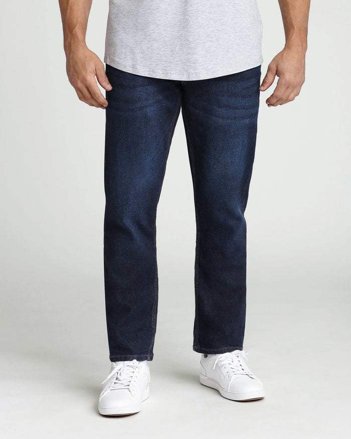 Man wearing light gray t-shirt and dark blue denim jeans with white sneakers.