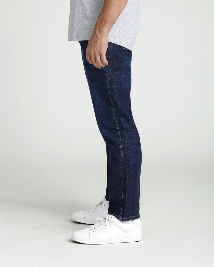 Dark blue athletic fit jeans on a model wearing a gray shirt and white sneakers.