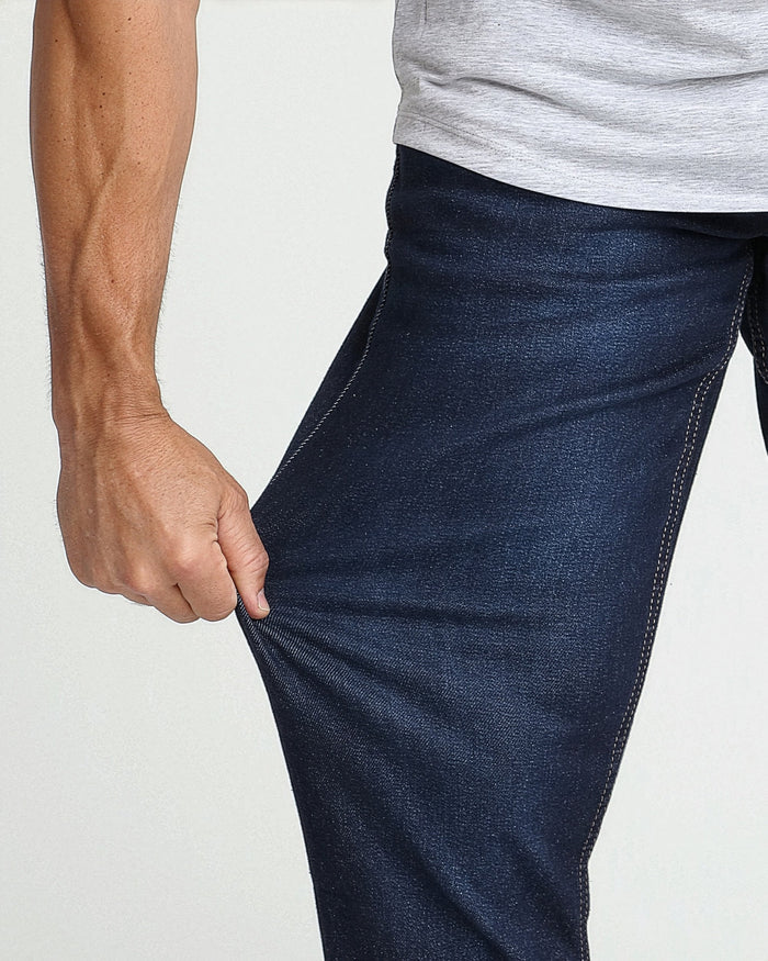 Man wearing dark blue athletic fit jeans with visible contrast stitching and gray t-shirt.