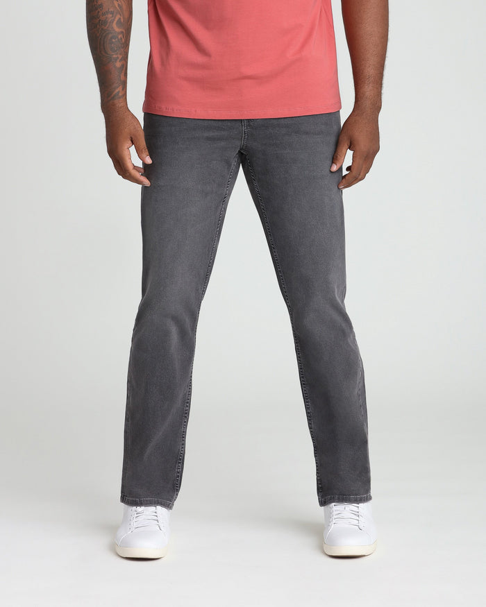 Man wearing coral t-shirt and gray athletic fit jeans with white sneakers.