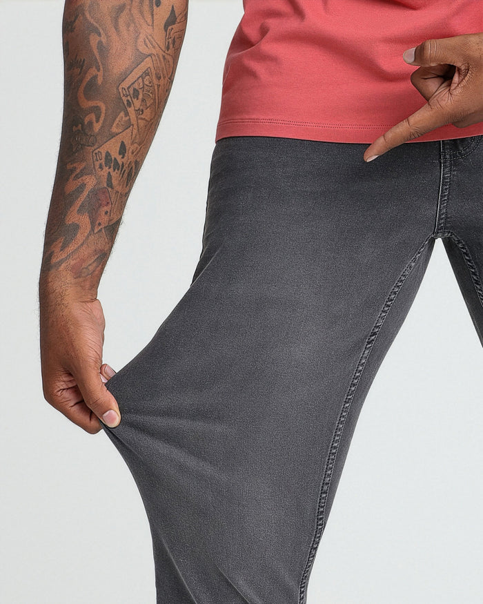 Grey denim jeans with athletic fit shown with pink t-shirt on model with tattooed arm.