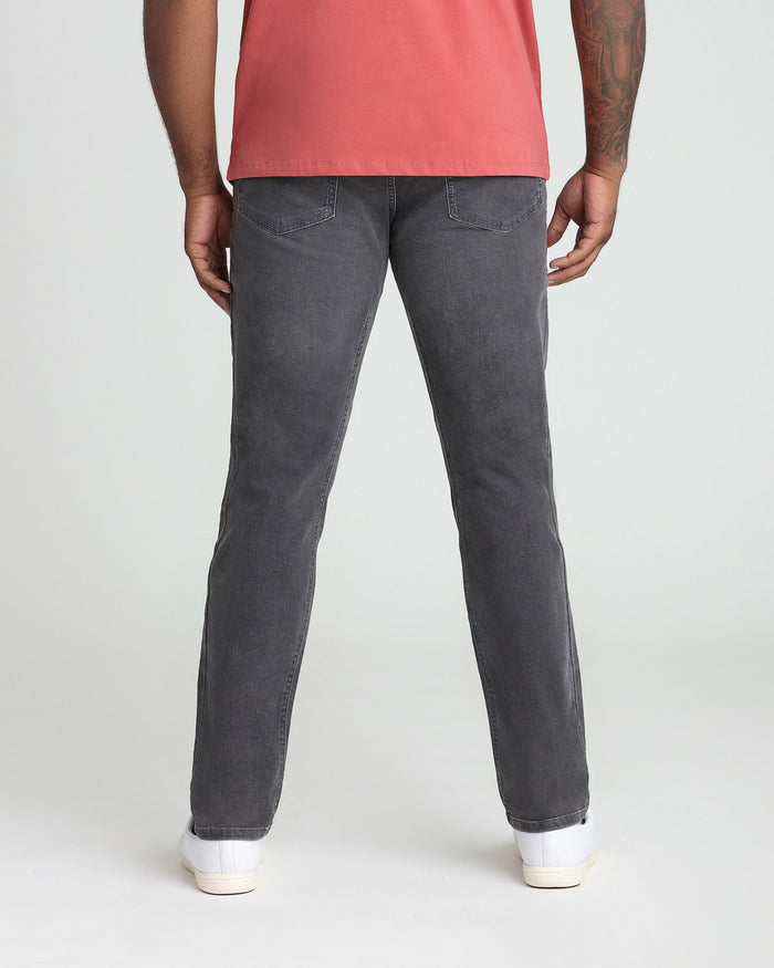 Man wearing grey athletic fit jeans with red t-shirt and white sneakers, shown from behind.