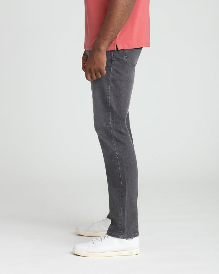 Man wearing grey athletic fit jeans with coral pink shirt and white sneakers.