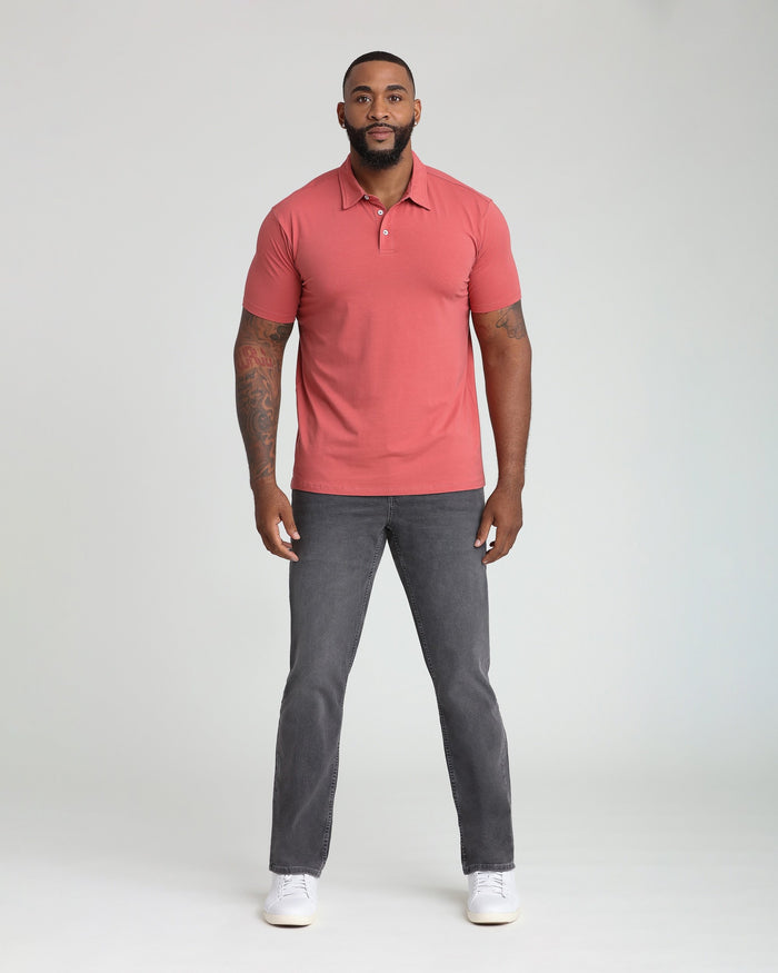 Man wearing coral polo shirt with collar and buttons, paired with charcoal gray jeans.