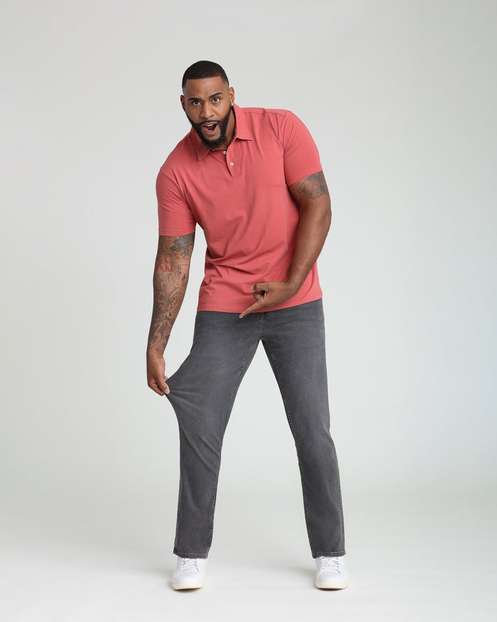 Man wearing coral polo shirt and grey athletic fit jeans with white sneakers.