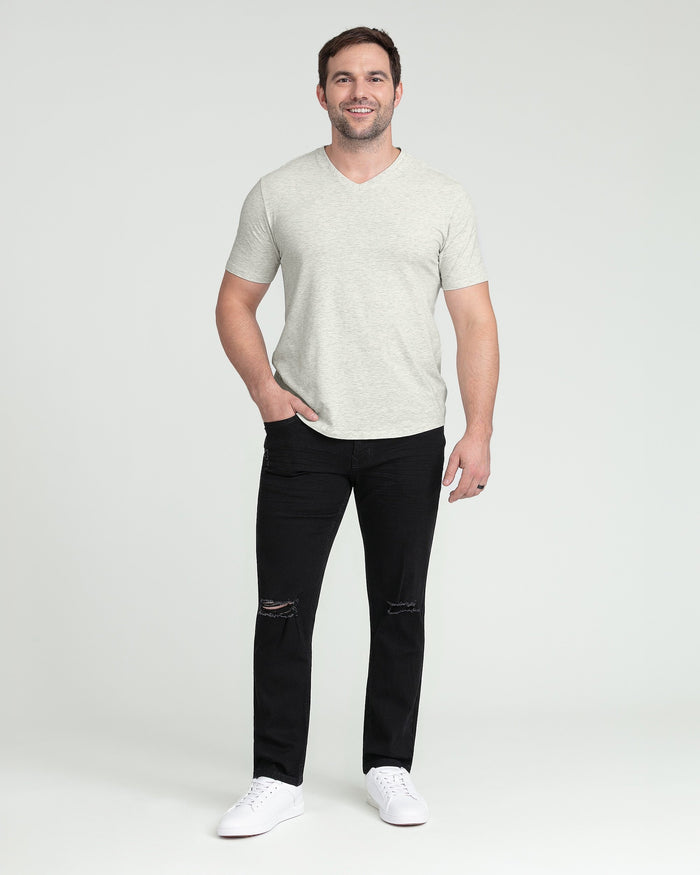 Man wearing light gray v-neck t-shirt and black ripped jeans with white sneakers.