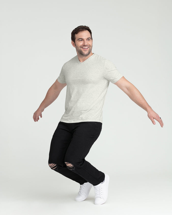 Man wearing gray V-neck t-shirt and black ripped jeans with white sneakers.