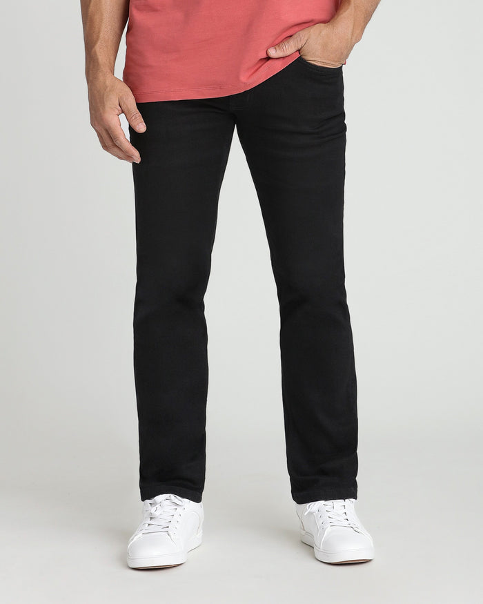 Black athletic fit jeans on model wearing coral shirt and white sneakers.