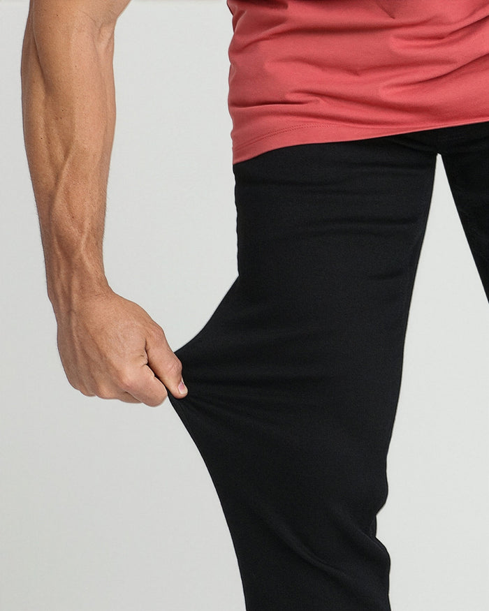 Man wearing coral pink sleeveless top and black athletic fit pants with hand in pocket.