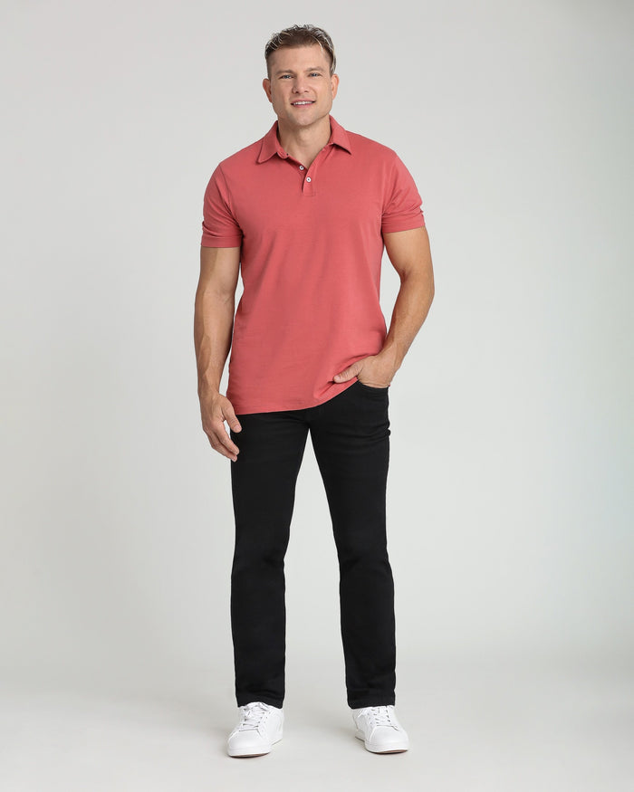 Man wearing coral pink short-sleeve polo shirt and black pants with white sneakers.
