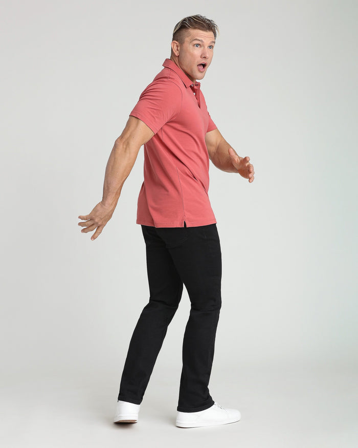 Man wearing coral short-sleeve polo shirt and black athletic pants with white sneakers.