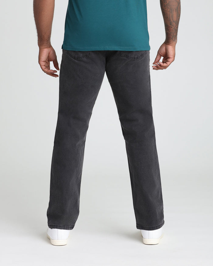Man wearing teal shirt and faded black athletic fit jeans with white sneakers, rear view.