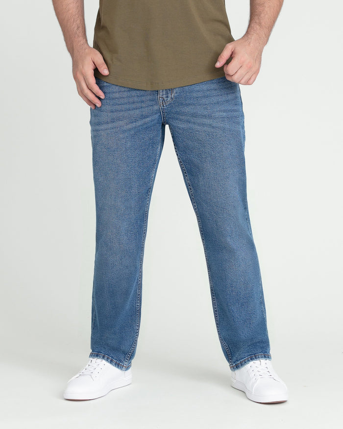 Man wearing medium blue denim jeans with athletic fit and olive green t-shirt, white sneakers.